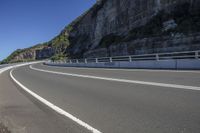 a car is driving along a curving road near mountains and a cliff at the background