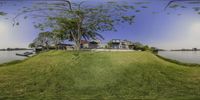 an oval lens of some trees by the water and green grass with two houses on it