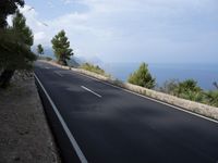 a car is driving down the middle of a road next to a sea and a hill