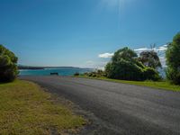 empty roadway by the beach with green grass and trees near by on hill at top