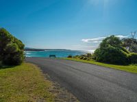 empty roadway by the beach with green grass and trees near by on hill at top