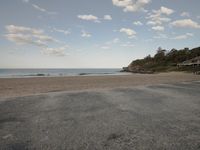 a empty road next to a beach under clouds in the sky and water near the shore