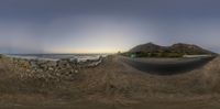 a fish eye lens of a road in the sand next to a beach with a house and mountains