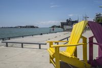 colorful wooden chairs are placed next to the water in front of a dock, while buildings are on the other side