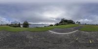 a panorama fish eye shot with the view down a road next to the beach and trees