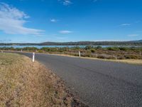 an empty country road next to the water with trees on the other side of it