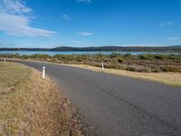 an empty country road next to the water with trees on the other side of it