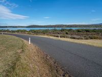 an empty country road next to the water with trees on the other side of it