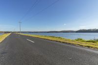 an empty road in the foreground of a body of water on a sunny day