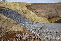 a pile of rocks and gravel beside some road tracks and a mountain behind it, with some dirt on the sides