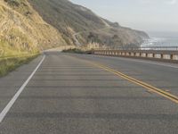 a motorcycle is riding on the road by the ocean and cliffs in the background with waves on the sea