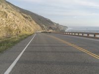 a motorcycle is riding on the road by the ocean and cliffs in the background with waves on the sea