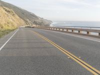 a motorcycle is riding on the road by the ocean and cliffs in the background with waves on the sea