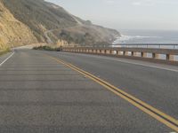 a motorcycle is riding on the road by the ocean and cliffs in the background with waves on the sea