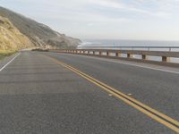 a motorcycle is riding on the road by the ocean and cliffs in the background with waves on the sea