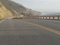 a motorcycle is riding on the road by the ocean and cliffs in the background with waves on the sea