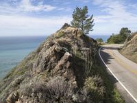 a motorcycle is resting on the rocky side of a hill near the ocean with trees