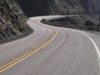 an empty long straight highway passes by on a cloudy day under a mountain range with large rocks and cliffs