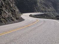 an empty long straight highway passes by on a cloudy day under a mountain range with large rocks and cliffs