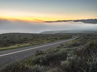 a man riding on the side of a road at dusk with fog covering the valley floor