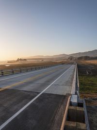 an empty road near the coast is lit by the setting sun with a mountain view