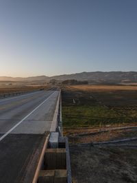 an empty road near the coast is lit by the setting sun with a mountain view