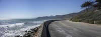 a paved stretch of road surrounded by a rocky shoreline with waves rolling up the side