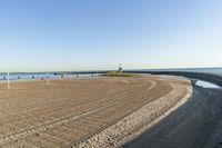 a wide expanse of sand at a beach area next to the ocean and pier with an empty blue sky