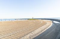 a wide expanse of sand at a beach area next to the ocean and pier with an empty blue sky