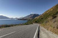 a country road with a scenic view of the lake and mountains in new zealand under a clear, cloudless sky