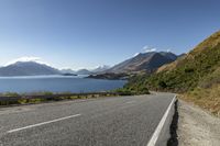 a country road with a scenic view of the lake and mountains in new zealand under a clear, cloudless sky