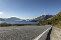 a country road with a scenic view of the lake and mountains in new zealand under a clear, cloudless sky