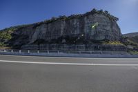 a winding road leading to large cliff formations by the side of it with one car moving in opposite direction