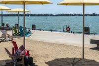 two large yellow umbrellas sit at the end of a sidewalk on a lakefront