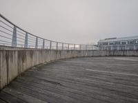 a long concrete sidewalk with a wooden walkway by it's railing and a building near the water