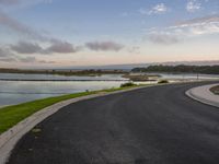 a road in the country next to water and a grass area with small bushes on either side of it