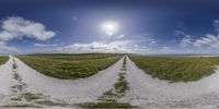 a road going down a dirt road near a field with clouds in the background and sun