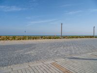 two people standing on the brick ground playing with a kite in the distance on an oceanfront