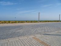 two people standing on the brick ground playing with a kite in the distance on an oceanfront