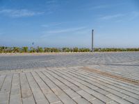 two people standing on the brick ground playing with a kite in the distance on an oceanfront