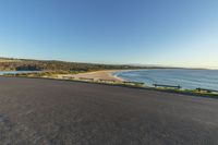 the road near the beach is empty as a person walks on it and takes their phone to the right