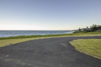 the empty street is next to the water and grass in the foreground is an oval area with a sandy beach near it