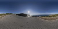 this is a fish eye lens of a road near the ocean in france, with a sun shining behind the road