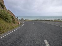 an empty paved road with ocean in the background and rocks out front with clouds in a low sky