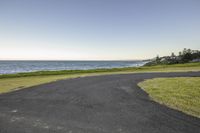 a road next to a grassy area near the water with a beach in the background