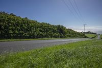 a road leading to a grassy hillside on a sunny day with a car parked at the roadside