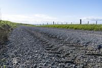 gravel road leading to grassy grass and field with barbed fenced in in area of large expanse