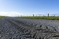 gravel road leading to grassy grass and field with barbed fenced in in area of large expanse