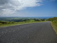 a lone street winding up the mountain side towards the ocean in the distance, the ocean, the sky, and grassy green hills