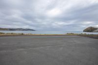 an empty parking lot near the water and mountains on a cloudy day in new zealand